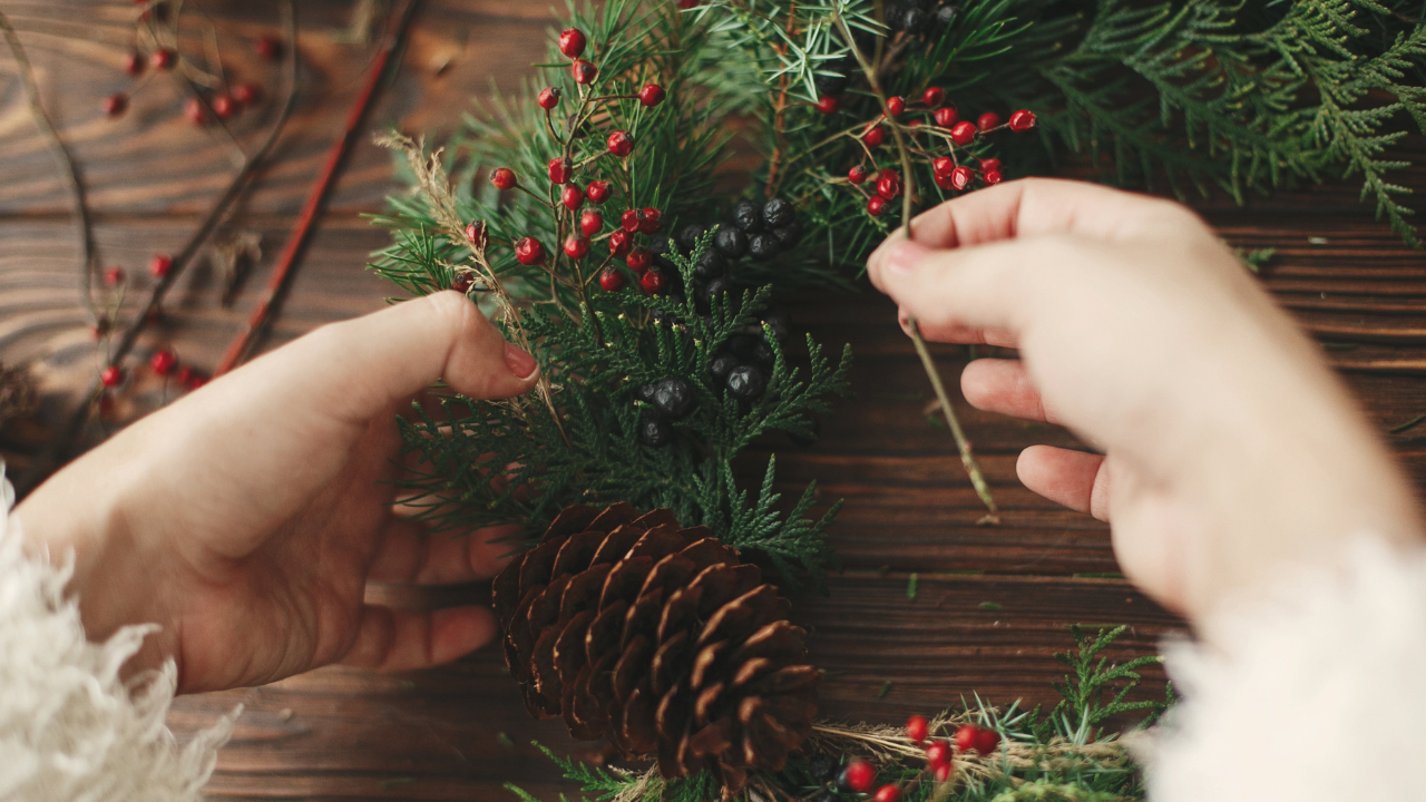 Hand gestaltet einen Adventskranz mit Tannenzweigen, Beeren und Zapfen im Adventskranz Workshop Hannover.